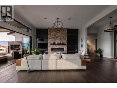 Sophisticated open-concept living. Features soaring wood-accent panels, a custom gas fireplace, and massive eclipse doors, framing panoramic valley and city views.