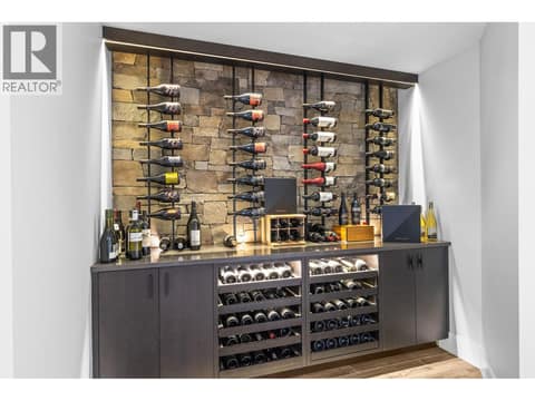 Custom wine cellar storage featuring wall-mounted wine racks against a natural stone accent wall, dark lower cabinetry, and built-in horizontal bottle display shelves. at 162 Skyland Drive, Wilden, Kelowna