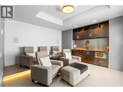 Luxury home theater room featuring two tiers of plush recliner seating with step lighting, a tray ceiling, and a built-in wet bar with dark wood cabinetry, tile backsplash, and a built-in microwave. at 162 Skyland Drive, Wilden, Kelowna