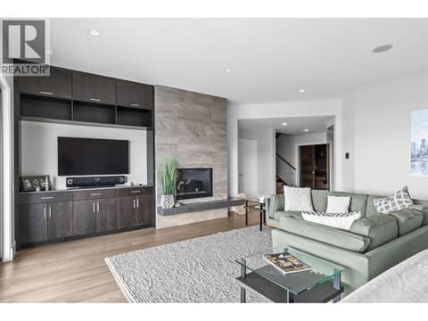 Modern walkout basement recreation room showing a large built-in entertainment unit with a wall-mounted TV, a floor-to-ceiling tile fireplace, and engineered hardwood flooring. at 162 Skyland Drive, Wilden, Kelowna
