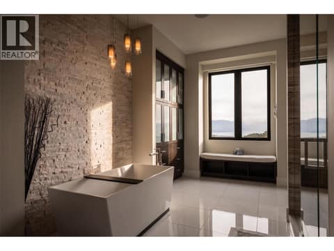 Spa-like luxury ensuite. Relaxing retreat featuring a deep standalone soaking tub, textured stone feature wall, custom glass steam shower, and large windows to capture the view at 162 Skyland Drive, Wilden, Kelowna