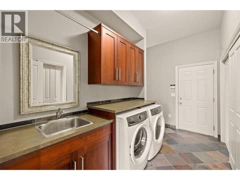 Main floor laundry with sink, storage, garage access and staircase to the lower level. at 10726 Nighthawk Road Unit# 60, Lake Country North West