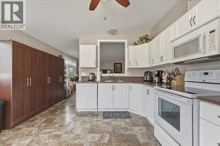 Storage cabinets on left provide extra storage, and pass through window to living room creates connection at 12560 Westside Road Unit# 77, Swan Lake West, Vernon