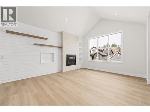 Living Room | Upper Level - soaring vaulted & open-to-below ceilings, wide-plank flooring, custom white-oak details and a Napoleon fireplace with full-height plaster surround at 1448 Whistling Pine Place, Wilden, Kelowna