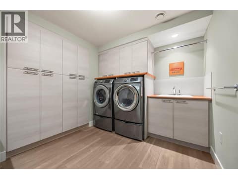 Lower level Laundry room with built in cabinetry, front loading washer and dryer and sink at 2442 Bella Vista Street, Black Mountain, Kelowna