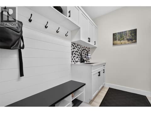 Functional mudroom off the garage with a built-in bench, storage, hooks and utility sink at 2400 Hawks Boulevard, Westbank Centre, West Kelowna