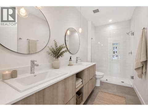 Spa inspired ensuite with dual vanities, oversized glass shower, modern lighting and warm wood cabinetry. *virtually staged at 3699 Capozzi Road Unit# PH6, Lower Mission, Kelowna