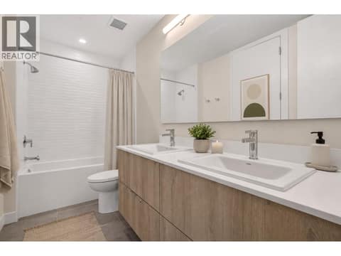 Well appointed second bathroom with dual sinks, full tub and shower, modern tile detail and warm wood cabinetry. *virtually staged at 3699 Capozzi Road Unit# PH6, Lower Mission, Kelowna