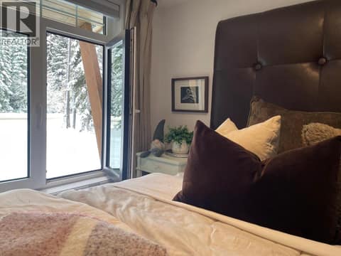 Bedroom with large windows overlooking snow-covered trees at 1166 Apex Mountain Road, Penticton Apex
