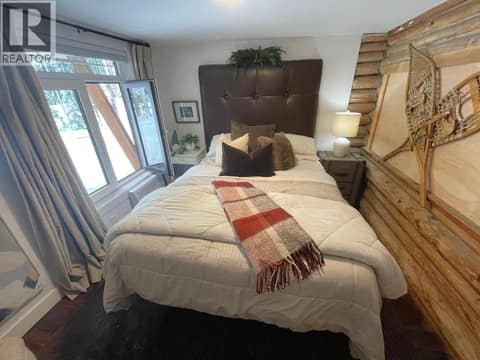 Main-floor bedroom with log accent wall and exterior windows at 1166 Apex Mountain Road, Penticton Apex