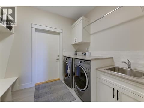 Laundry with front load washer and dry plus laundry sink and cabinets for storage at 13371 Apex Lane, Lake Country East / Oyama